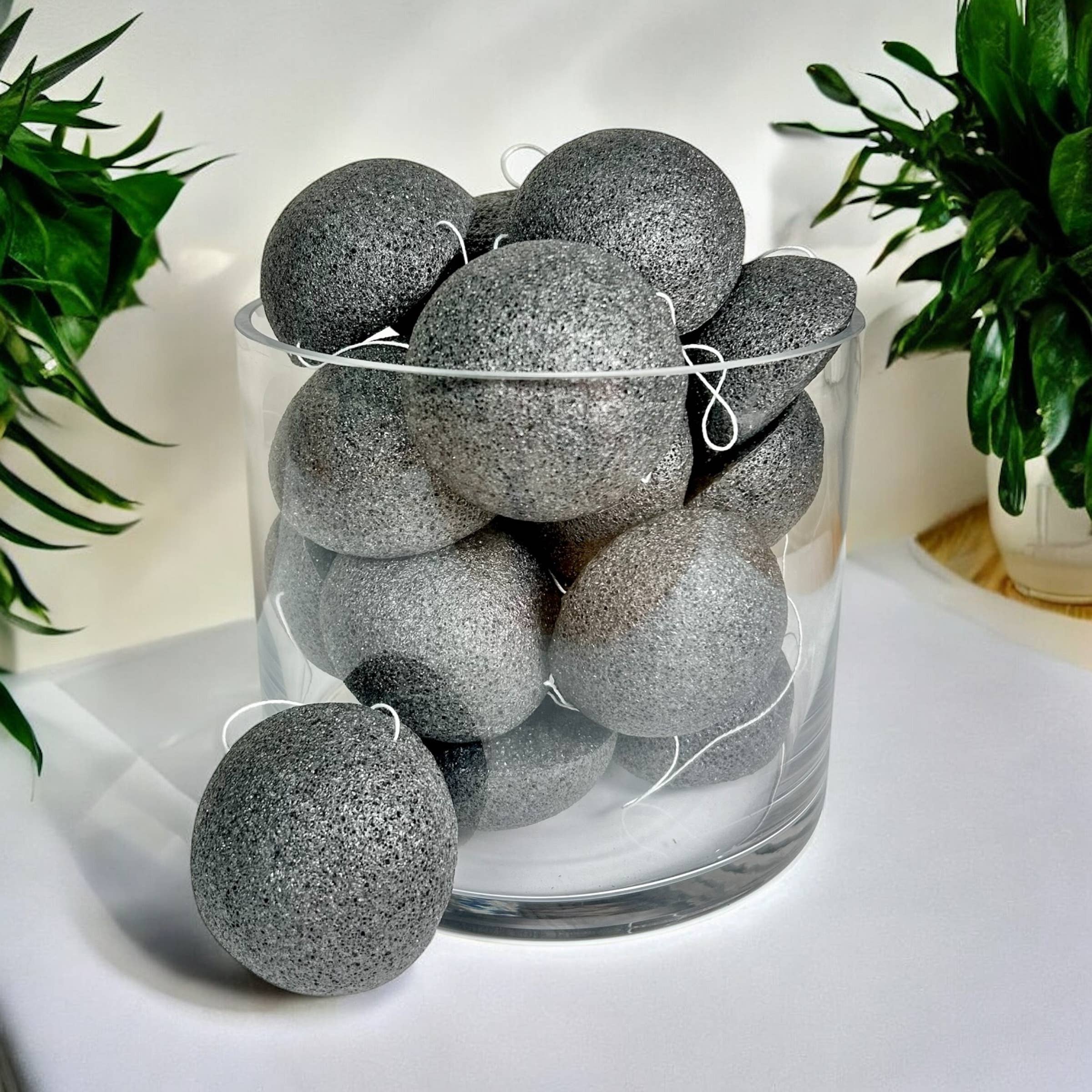 Glass vase filled with gray textured balls on a white surface with plants in the background